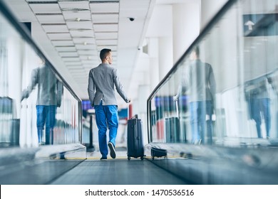 Well Dressed Young Man Travel By Airplane. Businessman With Luggage Walking On Travelator At Airport.