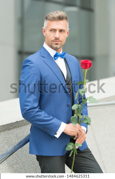 Well groomed macho tailored suit. Make good first\
impression. Valentines day and anniversary. Romantic gentleman. Man\
mature confident macho with romantic gift. Handsome guy rose flower\
romantic date.