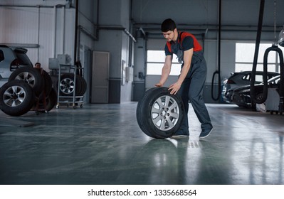 We'll make it quick. Mechanic holding a tire at the repair garage. Replacement of winter and summer tires.