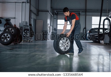 We'll make it quick. Mechanic holding a tire at the repair garage. Replacement of winter and summer tires.