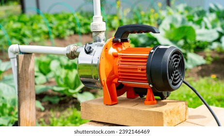 Well on plot, orange water pump for irrigation of vegetable garden, water pump in country
