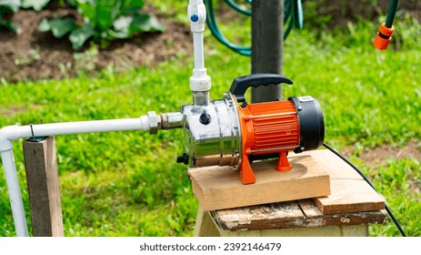 Well on plot, orange water pump for irrigation of vegetable garden, water pump in country