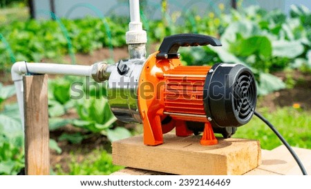 Well on plot, orange water pump for irrigation of vegetable garden, water pump in country