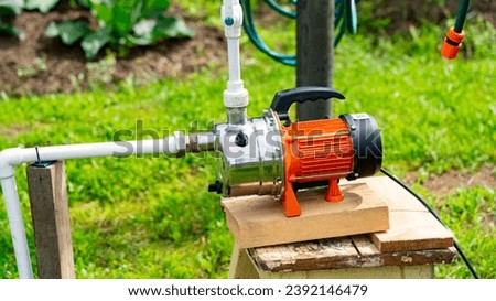 Well on plot, orange water pump for irrigation of vegetable garden, water pump in country