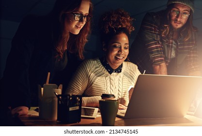 Well Succeed Together. Shot Of A Business Team Using A Laptop Together On A Night Shift At Work.