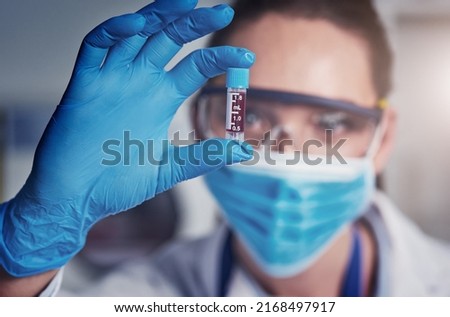 Well this took a long while to achieve. Closeup of an unrecognizable female scientist wearing a protective face mask and holding up a vile of blood inside of a laboratory.