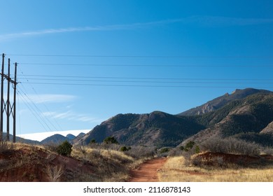 Well Worn Path Of Red Dirt Beneath Overhead Power Lines, View Of The Rocky Mountains Beyond On A Clear Morning, Horizontal Aspect