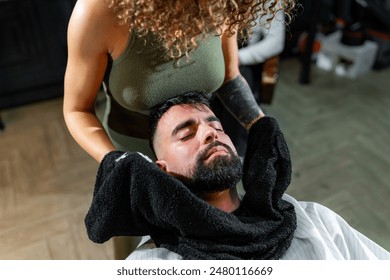 In a well-appointed barbershop, a man receives a hot towel facial treatment from a skilled barber, part of an upscale grooming ritual focusing on man’s skincare and relaxation. - Powered by Shutterstock