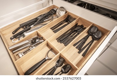 A well-arranged kitchen drawer showcases an assortment of utensils, cutlery, and tools, emphasizing cleanliness and modern organization within a sleek wooden divider. - Powered by Shutterstock