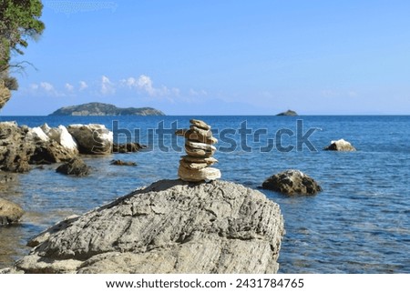 Well-balanced stack of rocks on a large, rough boulder on a beach on Skiathos island, Greece. Backdropped by the bright, calm aegean sea and a clear blue sky.