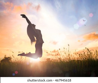 Wohlbefinden: Silhouette einer glücklichen Frau, die mit ihren Händen springt, die auf orangefarbenem, herbstlicher Naturhintergrund erhoben werden