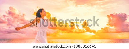 Wellbeing freedom happy woman jumping dancing of joy with open arms in the air blissful banner. Asian woman in sunset clouds pink sky background.