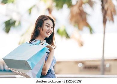 Wellbeing single lifestyle on holidays. Happy young adult southeast asian woman with shopping bags on day. Wear blue shirt with long hair. - Shutterstock ID 2152520139