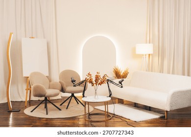A well-designed podcast studio features two comfortable chairs and a white sofa. Modern microphones are positioned on a small table. Natural light and decor create a welcoming atmosphere.