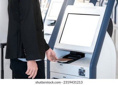 Well-dressed Businessman passenger using self service machine and help desk kiosk at airport terminal for check in, print boarding pass or buying ticket. Business travel and holiday trip concepts