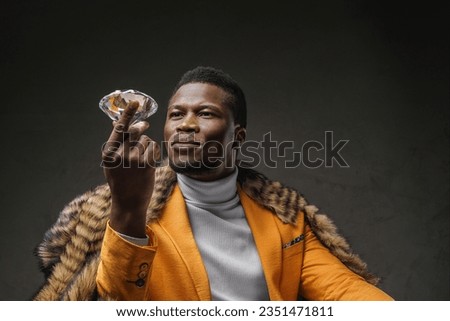 A well-dressed dark-skinned man holding a large diamond while draped in a wild animal skin on a textured background