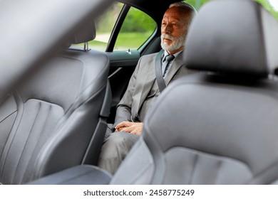 Well-dressed elderly man with a beard smiles contentedly while seated in the back of a modern vehicle - Powered by Shutterstock