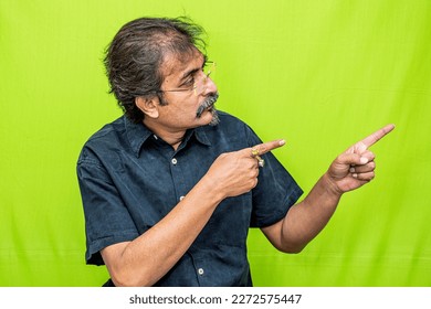 The well-dressed Indian man wearing a black shirt is pointing in the right direction with both of his hand's fingers while standing against a green screen background - Powered by Shutterstock