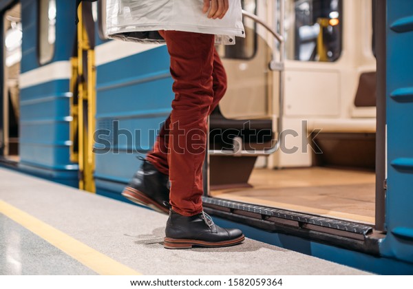 Well-dressed man in black shoes, red pants and\
white jacket enters into a subway train early in the morning. The\
left leg is blurred. Close up photo. Public transport and mobility\
in urban concept.