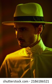 A Well-groomed Brutal Brunet Man In An Elegant White Shirt And Hat Stands In A Dark Room Looking Resolutely Away. Mafia And The Criminal World.