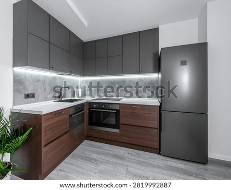 A well-lit, modern kitchen featuring dark gray cabinets, a stainless steel sink, and a black refrigerator. The space is complemented by wooden accents and a minimalist design.