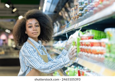 In a welllit supermarket aisle, a dedicated female employee with curly hair is diligently restocking shelves to ensure they are wellstocked and organized, delivering professional service to customers - Powered by Shutterstock