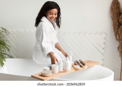 Wellness. African Lady Choosing Natural Cosmetic Products Caring For Herself Sitting On Bathtub In Bathroom Indoors. Woman Enjoying Beauty Routine In Spa Center. Selective Focus