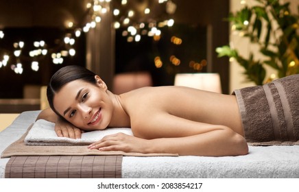 wellness, beauty and relaxation concept - young woman lying at spa or massage parlor over christmas lights on window background