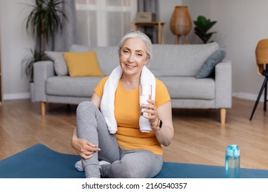 Wellness concept. Active senior woman drinking fresh water from glass after domestic sports workout, copy space. Sporty female staying hydrated during home fitness - Powered by Shutterstock