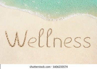 Wellness concept photo. Word Wellness handwritten on the sand. Beach and soft wave background.