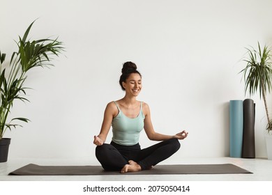 Wellness Concept. Smiling Young Lady Meditating On Yoga Mat At Home, Portrait Of Calm Relaxed Beautiful Brunette Woman Sitting In Lotus Position, Practicing Meditation In Light Room, Copy Space - Powered by Shutterstock