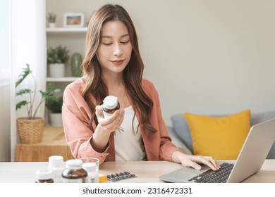 Wellness and dieting asian young woman, girl working from home using computer, typing or searching prescription on medicine label about vitamins information online, holding bottle of food supplement. - Powered by Shutterstock