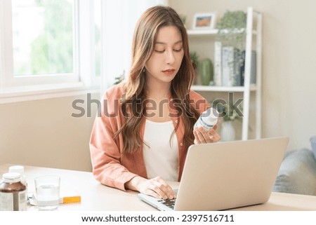 Wellness and dieting asian young woman, girl working from home using computer, typing or searching prescription on medicine label about vitamins information online, holding bottle of food supplement.