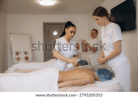 Wellness instructor demonstrating massage techniques and applying cream to a student during a professional spa training course in a bright room