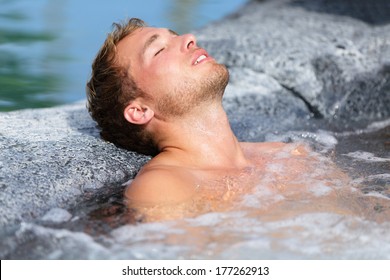 Wellness Spa - man relaxing in hot tub whirlpool Jacuzzi outdoor at luxury resort spa retreat. Handsome young male model relaxed with eyes closed resting in water near pool on travel vacation holiday.