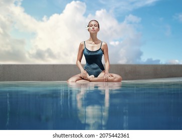 Wellness spa, vacation and yoga meditation concept. Pretty young woman in swimsuit sitting in lotus position near the swimming pool with sky behind her. - Powered by Shutterstock