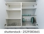 A wellorganized kitchen cabinet filled with neatly arranged plates, stylish cups, and elegant glasses, creating a functional and aesthetically pleasing space for dining essentials