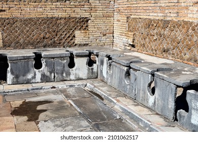 The well-preserved remains of an ancient Roman public bathroom with travertine seats and toilet drains, under the seats, the drains were constantly cleaned by a path of rough water, OstiaAntica