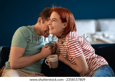 Well-rested couple talking and laughing. Middle aged smiling wife and husband sitting with cup tea morning on sofa. Loving family having fun weekend. Emotional connection in healthy relationship.