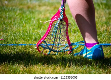 Wells, Maine, USA: June 15, 2018: A Closeup Shot Of A Lacrosse Stick Next To A Youth Wearing A Nike Cleat Shoe Against A Grass Background. The Concept Is The Nike Slogan Of “just Do It.”