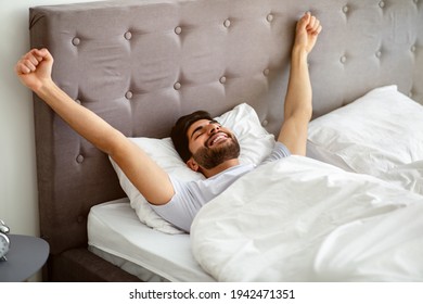 Wellslept Arab Guy Waking Up And Stretching Hands, Lying In Comfortable Bed With Eyes Closed