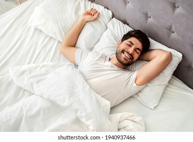 Wellslept arab man waking up and smiling, enjoying good morning in bed