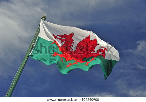 The Welsh flag against a blue\
sky. Motion blur at the tip of the flag. Space for text in the\
sky.