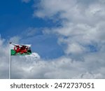 The Welsh national flag, isolated against a cloudy blue sky.