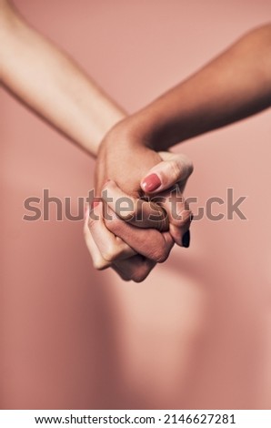Were capable of so much when we stand together. Shot of two unrecognizable women holding hands against a pink background.