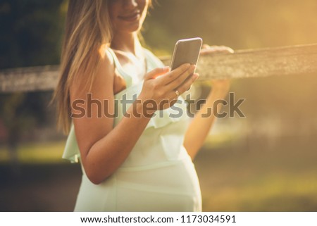 We're good  both the baby and me. Pregnant woman standing outside and using smart phone. Close up.