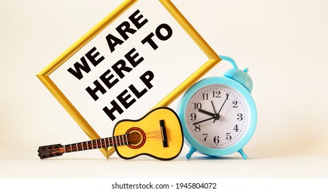 We're Here To Help Text On Photo Frame, Near Miniature Guitar And Alarm Clock .Business Concept