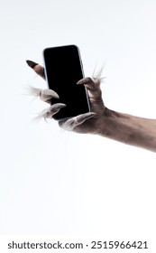 Werewolf's hand with long fingers and nails, paw holding modern smartphone with blank screen against white studio background. Concept of season sale, celebration, web. Negative space to insert text.