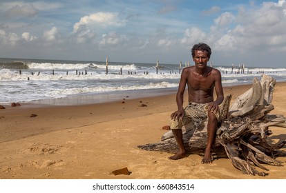 West Bengal, India, June 11, 2017: A rural fisherman pose for the camera sitting on an uprooted tree stem on the sea beach at Tajpur, West Bengal, India.