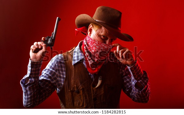 West, guns. American bandit in mask, western man with hat. Portrait of farmer or cowboy in hat. Portrait of a cowboy. American farmer. Portrait of man wearing cowboy hat, gun, macho.
